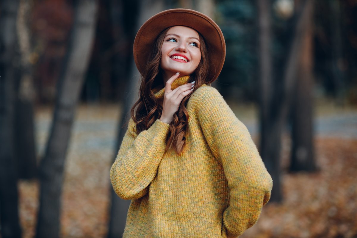 Smiling woman in a cosy yellow jumper in an autumn park