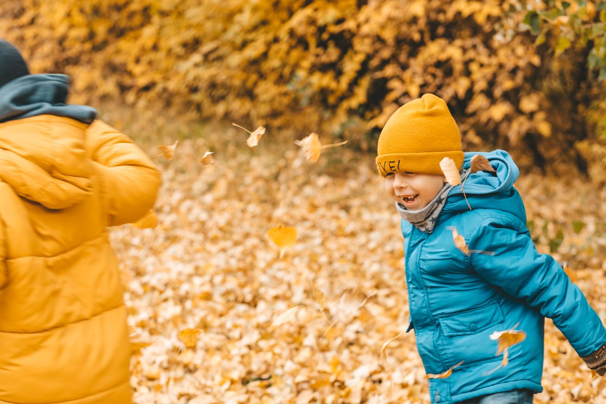 Kinderen spelen in herfstbladeren in warme jassen