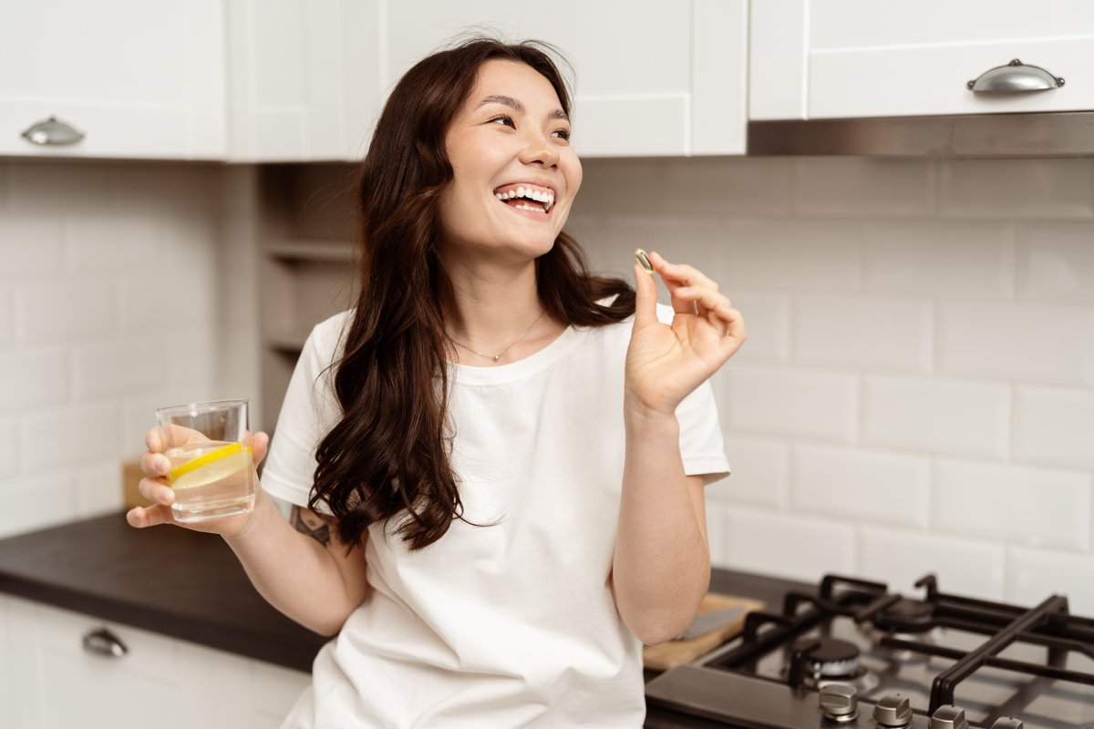 Woman smiling in her kitchen taking a vitamin with a glass of water