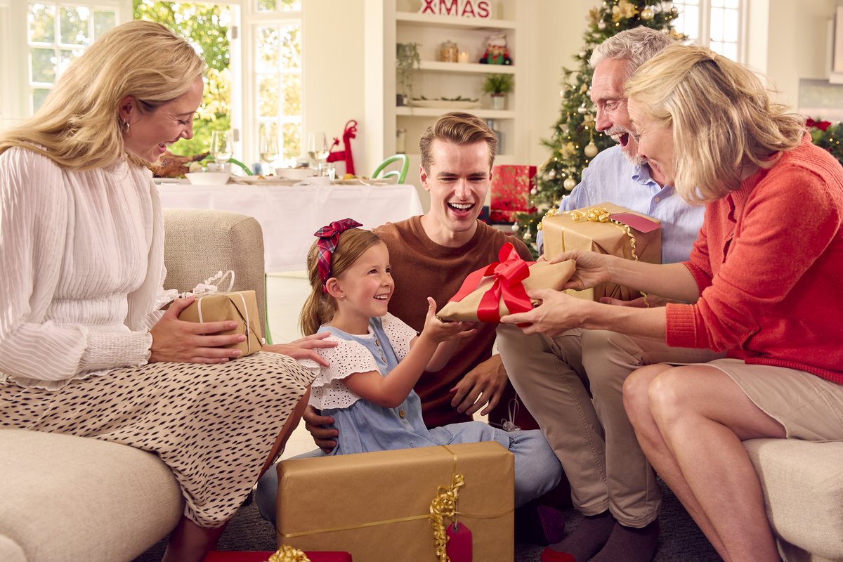 Smiling family opening gifts together on a sofa at home