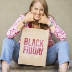Smiling woman sitting on steps holding a Black Friday shopping bag