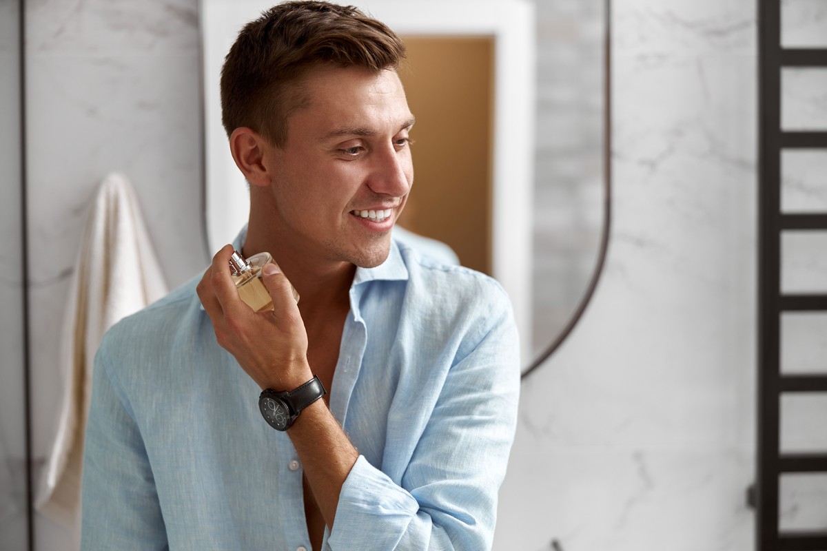 Smiling man applying cologne in a bathroom