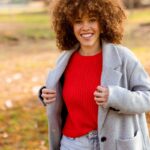 Femme souriante en pull rouge et manteau gris dans un parc en automne