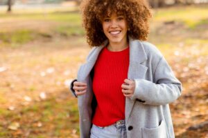 Femme souriante en pull rouge et manteau gris dans un parc en automne