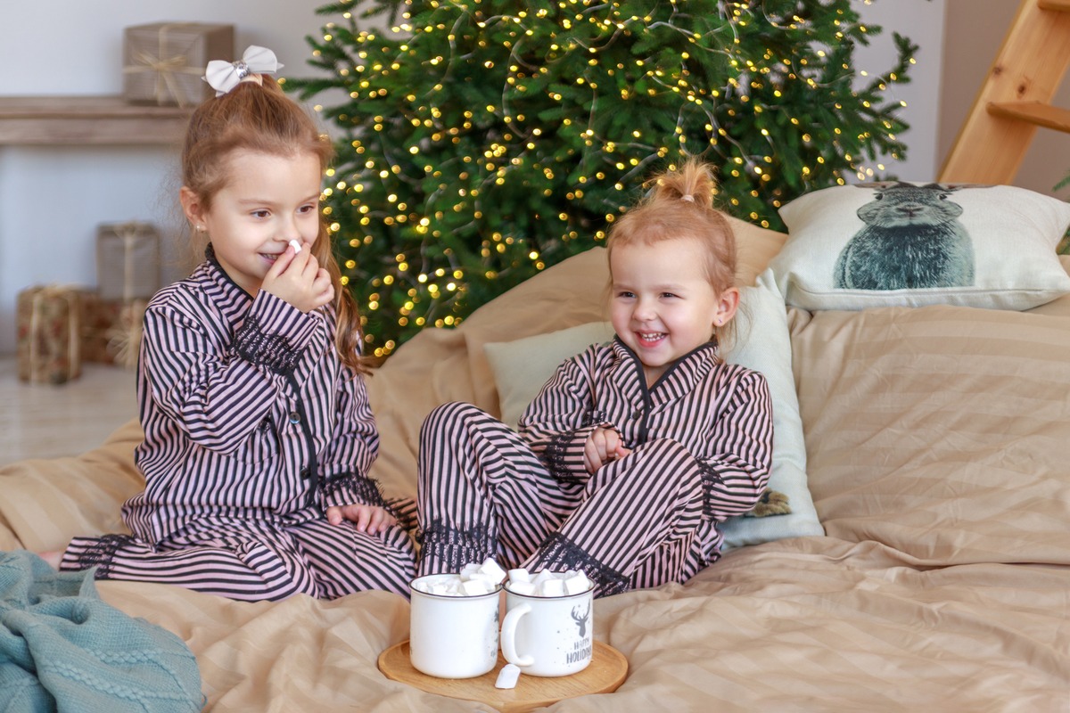 Deux fillettes en pyjama à rayures près du sapin de Noël avec un chocolat chaud