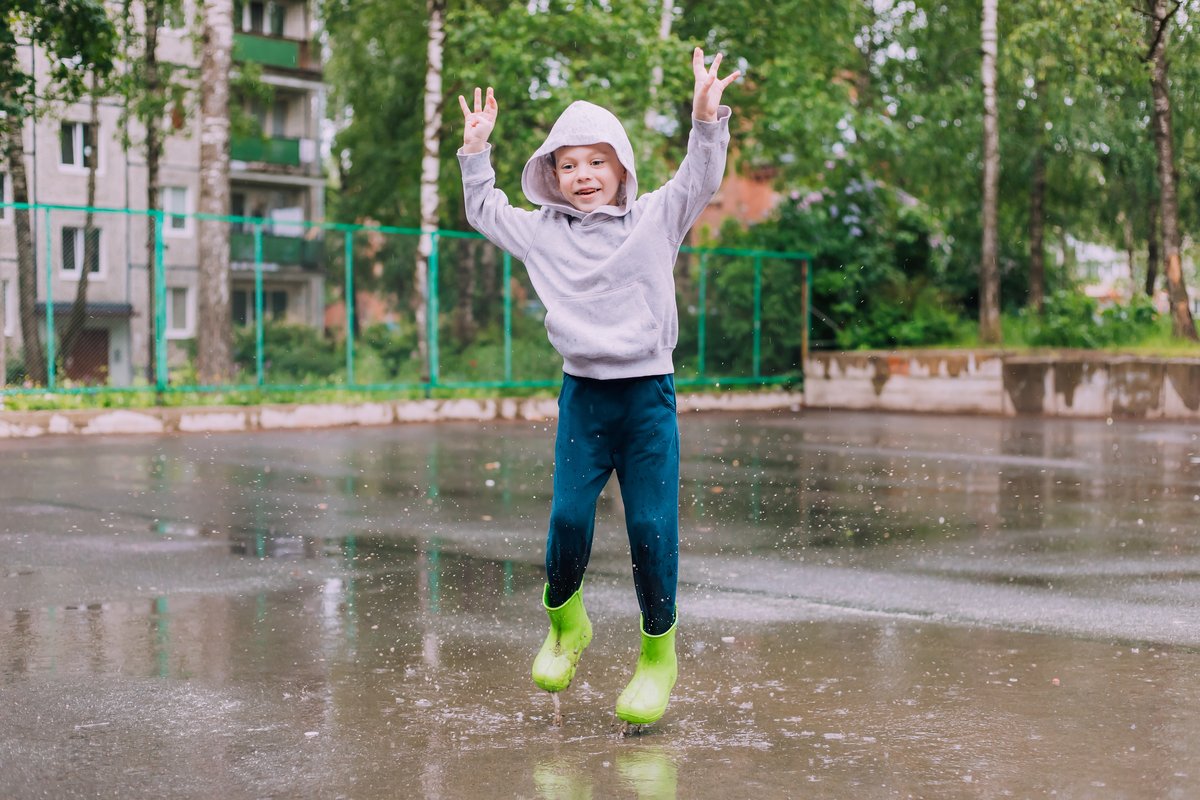 Lachend kind springt in een plas met groene regenlaarzen
