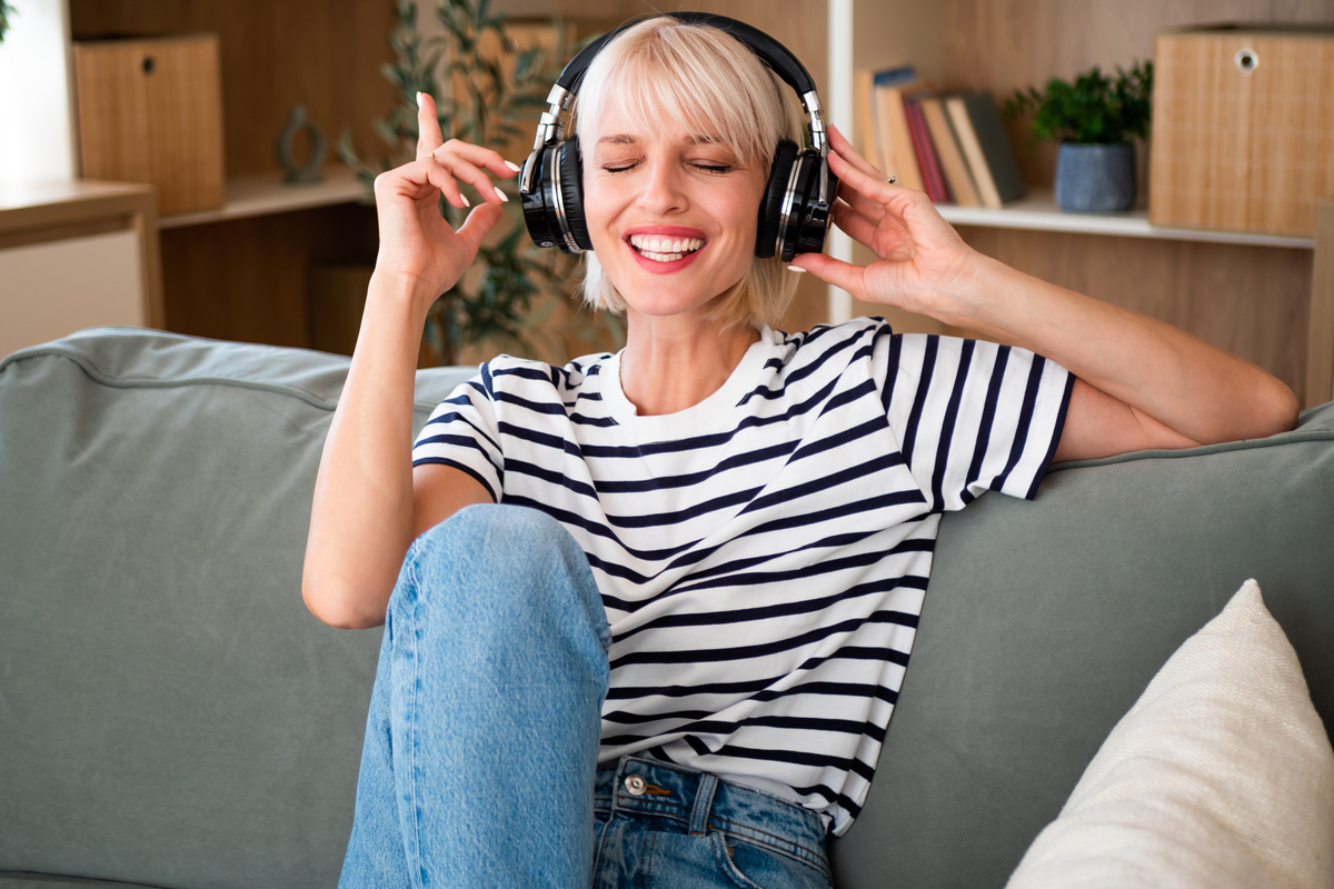 Lachende vrouw met een koptelefoon luistert thuis op de bank naar muziek