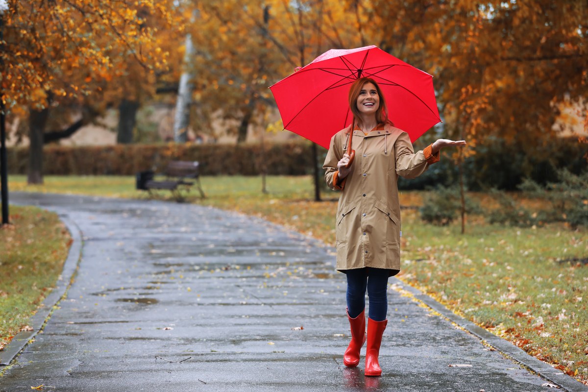 Smiling woman in a coat with a red umbrella on a rainy autumn day