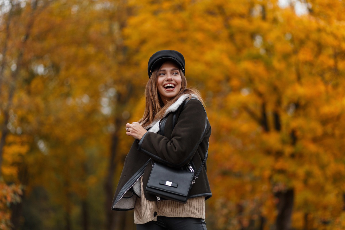 Smiling woman in an autumn park with a black shoulder bag