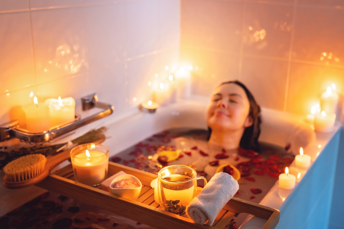 Woman relaxing in a candlelit bath with a tray of candles and tea