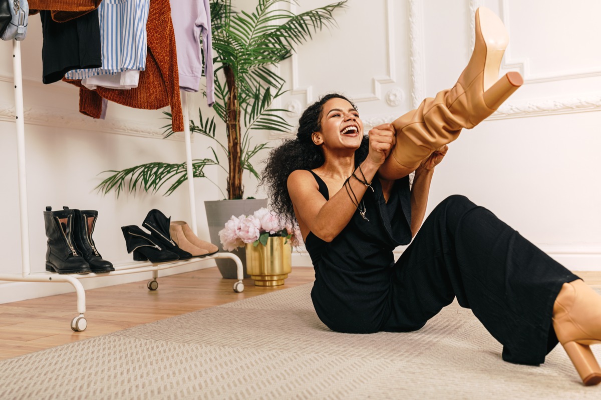 Laughing woman pulling on a tan boot in a bright room