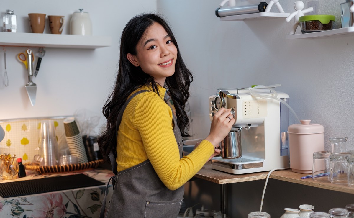 Smiling woman making coffee with a coffee machine in a bright kitchen