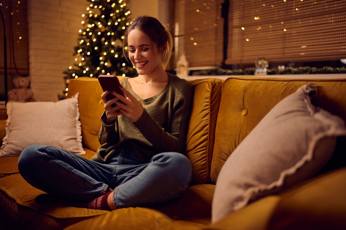 Smiling woman relaxing on a sofa next to a lit Christmas tree