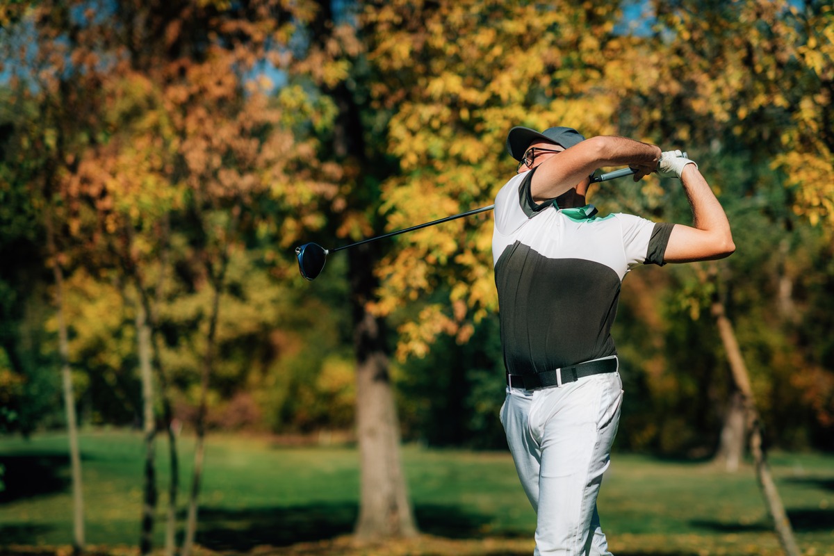 Golfer finishing a swing on a golf course surrounded by fall foliage
