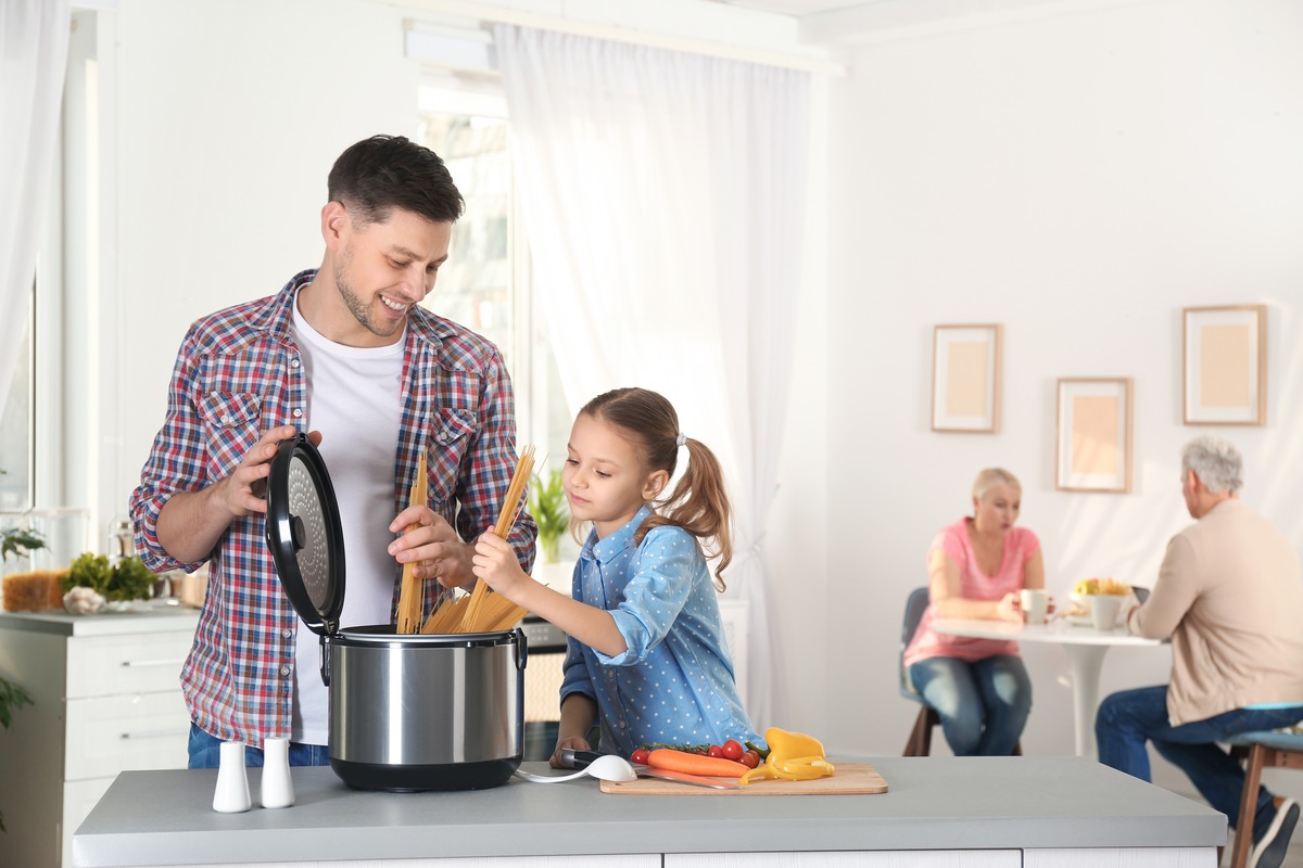 Father and daughter cooking together in a bright kitchen with a multi cooker